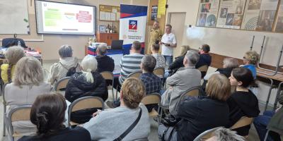 Na zdjęciu widoczna jest sala lekcyjna podczas szkolenia z zakresu ochrony ludności i obrony cywilnej organizowanego dla mieszkańców w Szkole Podstawowej nr 37 w Szczecinie. W pomieszczeniu siedzi około trzydziestu osób w różnym wieku, ustawionych na krzesłach w kilku rzędach i skierowanych w stronę prowadzących szkolenie.  Na przedzie sali znajdują się dwaj instruktorzy. Jeden z nich ubrany jest w jasną koszulkę z logo Szczecina, drugi w mundur służbowy. Obok nich ustawiony jest roll-up z herbem Szczecina 